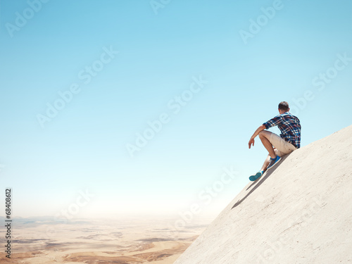 Young man sitting on a peak and desert