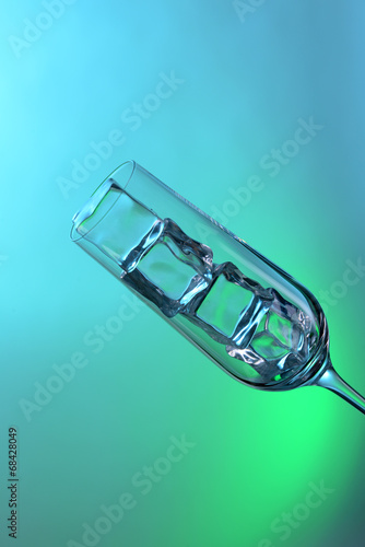 Glass with ice cubes on color background