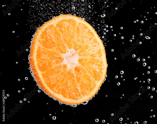 Fresh orange in water with bubbles on black background