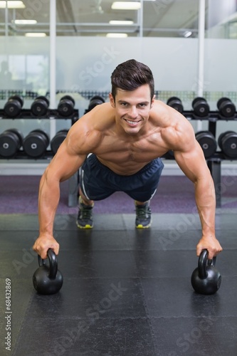 Muscular man doing push ups with kettle bells in gym