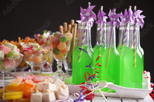 Bottles of drink with straw and sweets on dark background