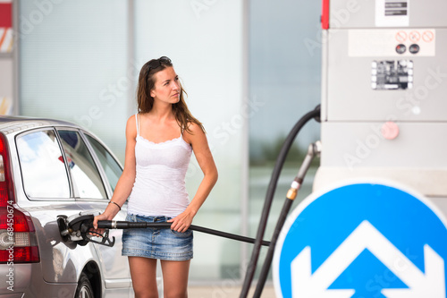 Attractive, young woman refueling her car in a gas station photo