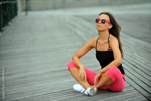 Sporty woman resting on the beach sitting on the boardwalk.