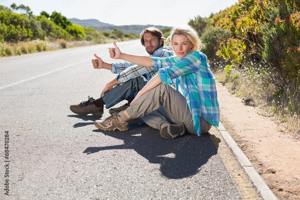 Obraz premium Attractive couple sitting on the road hitching a lift
