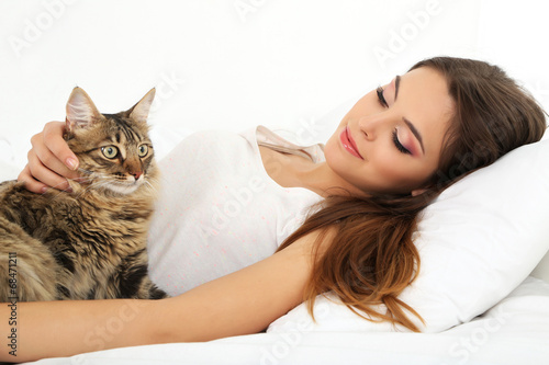 Beautiful young woman with cat resting on bed