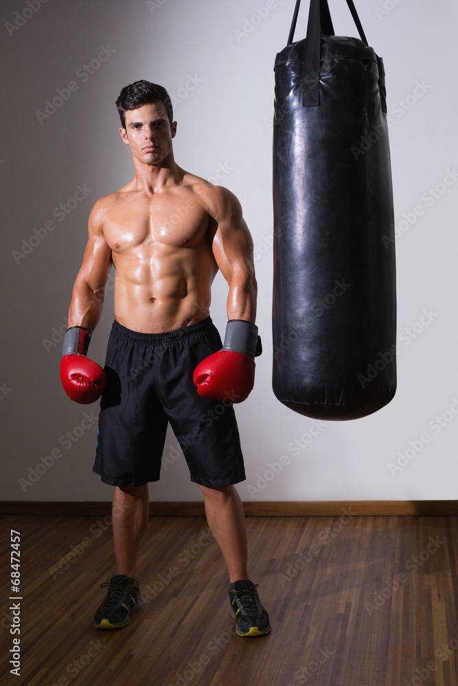 Shirtless muscular boxer with punching bag in gym Shirtless muscular boxer with punching bag in gym