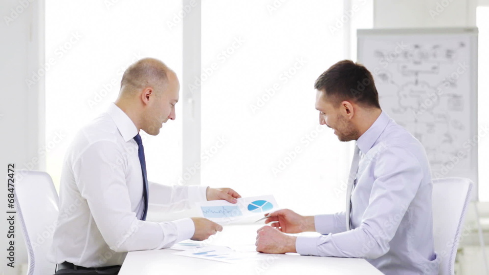 two smiling businessmen with charts in office two smiling businessmen with charts in office