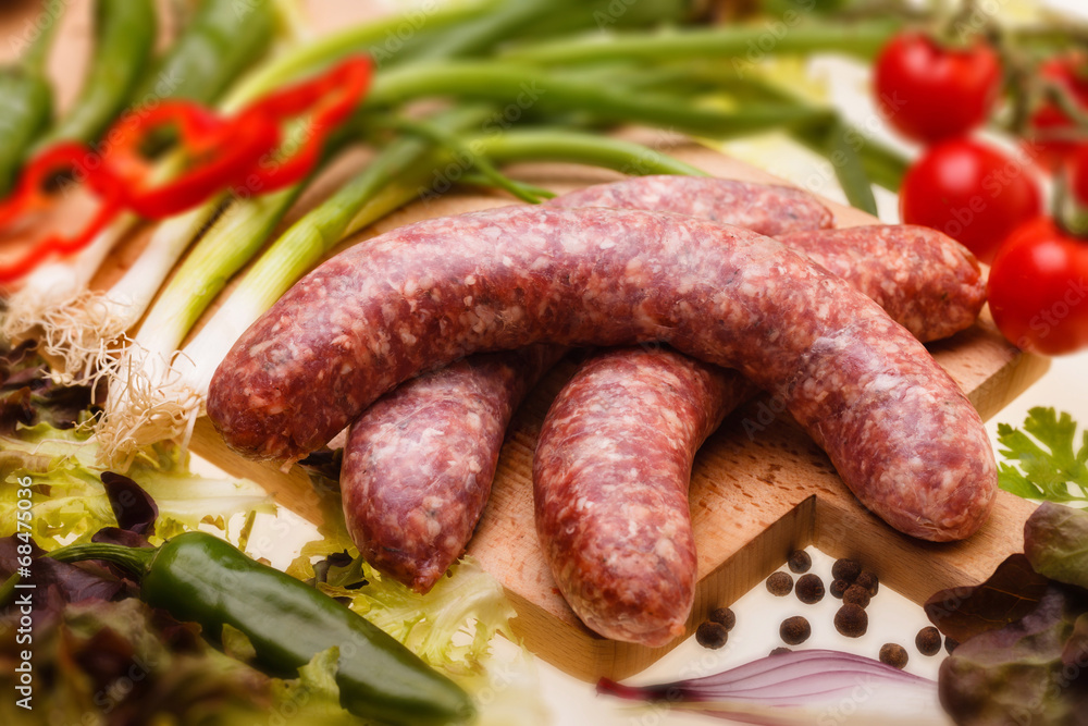 raw sausages with vegetables on wooden board