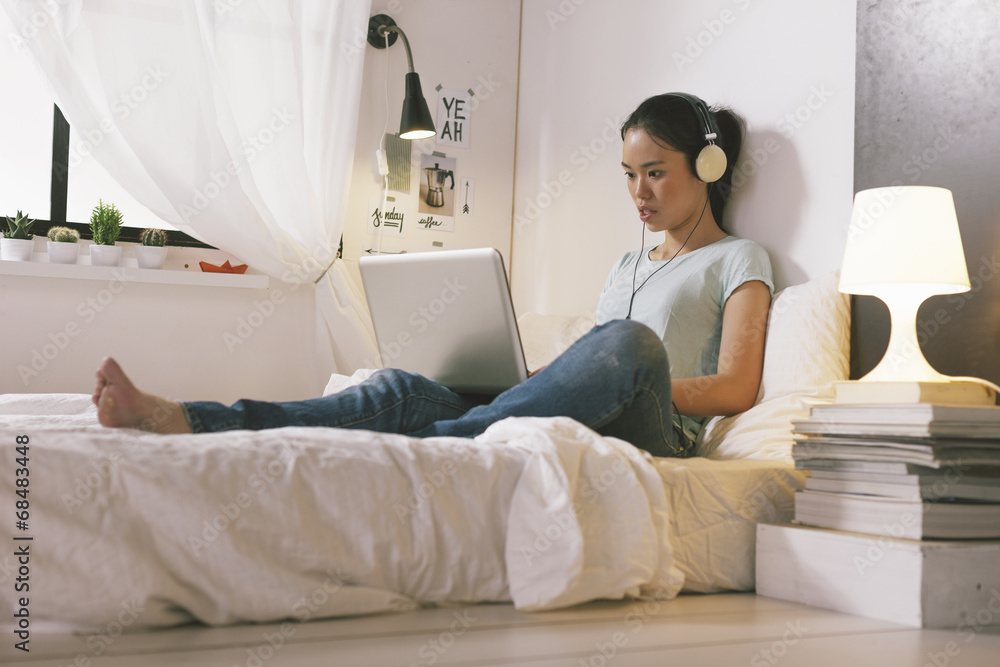 Casual young woman sitting on bed and using laptop at home. Casual young woman sitting on bed and using laptop at home.