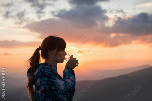 Woman drinking water on sunset background