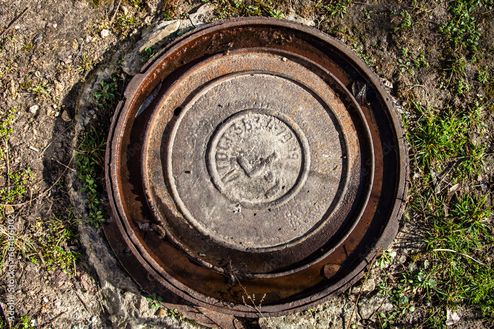 Manhole with rusty metal cover and water in its grooves