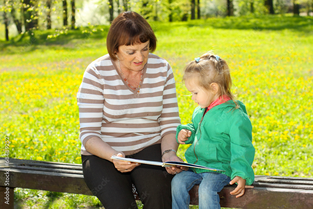 Grandmother and granddaughter reading a book outdoors Grandmother and granddaughter reading a book outdoors