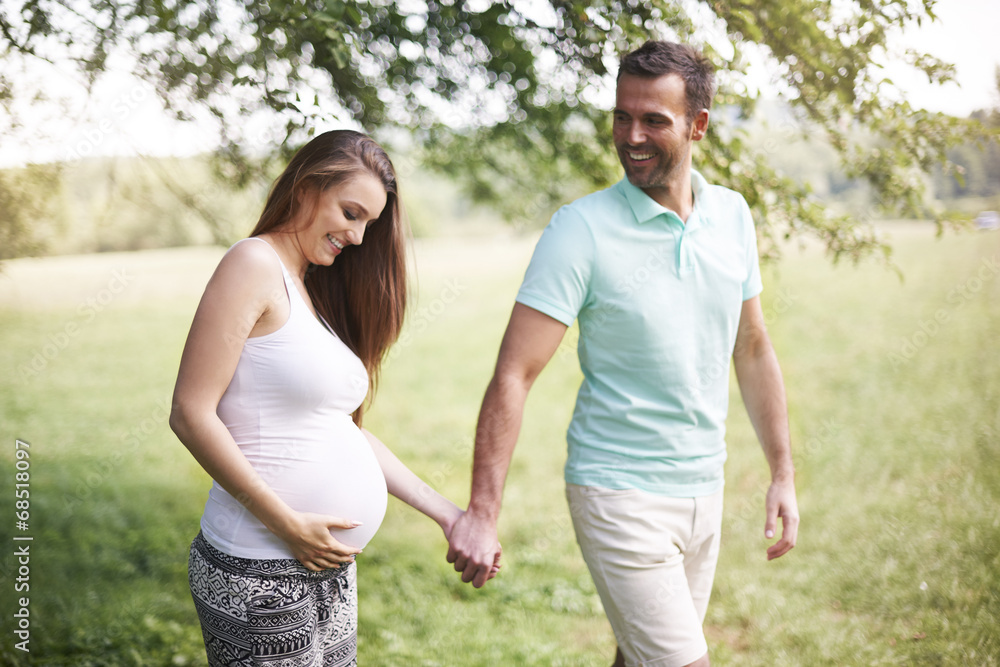 Pregnant woman with husband walking on meadow Pregnant woman with husband walking on meadow
