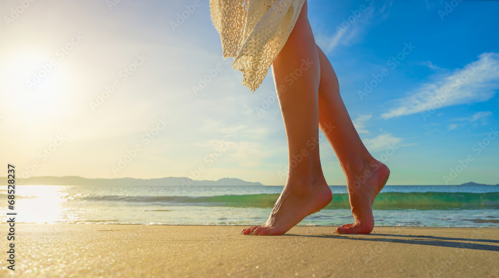 Young woman in white dress walking alone on beach in sunrise - obrazy, fototapety, plakaty 