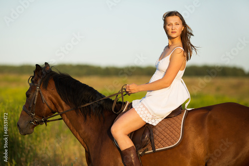 Girl in dress riding on a brown horse