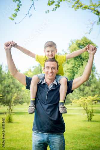Cheerful man carrying his son on back against park