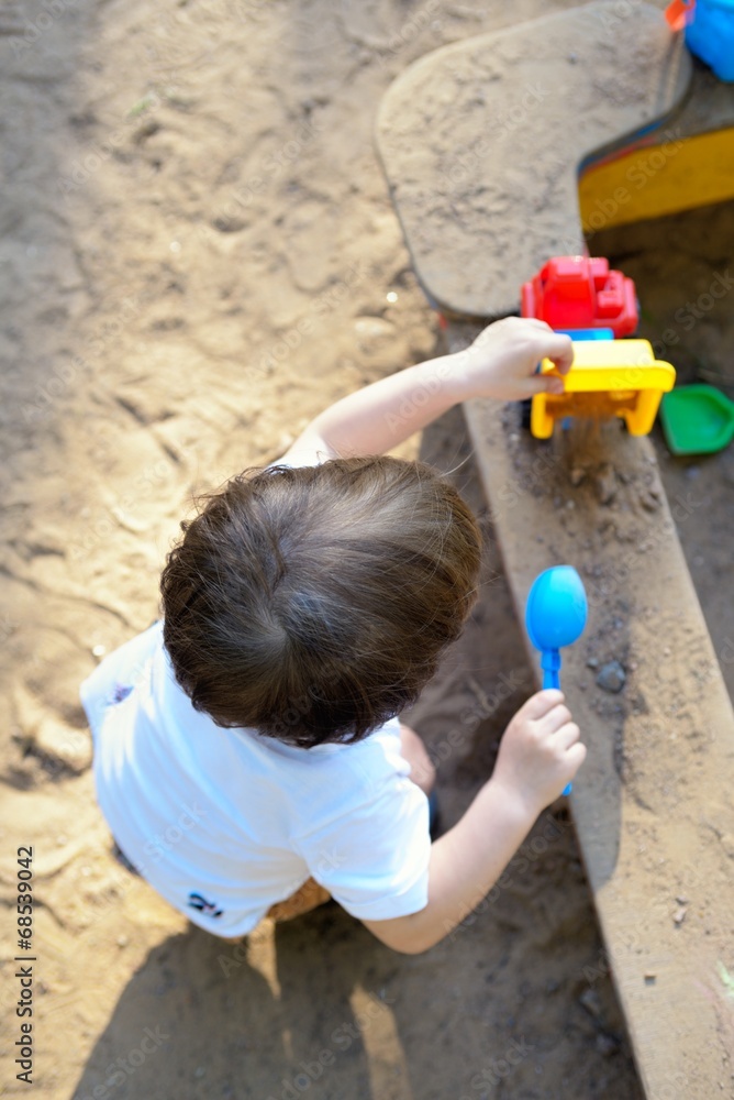 The small child plays in a sandbox with toys The small child plays in a sandbox with toys