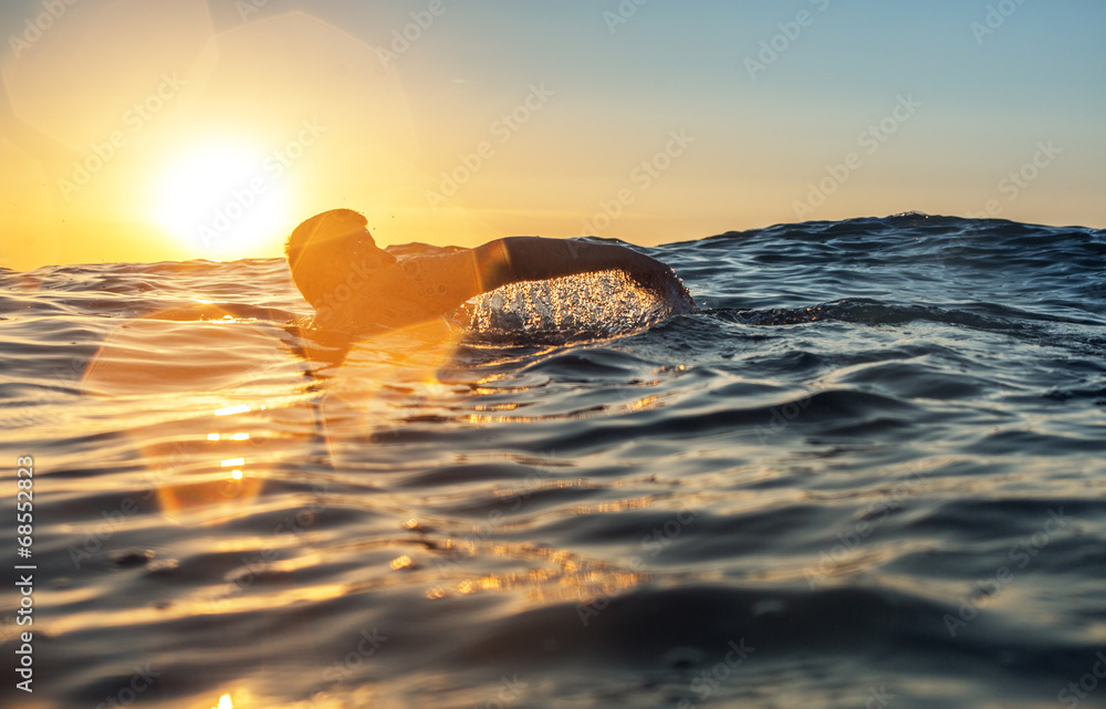 Fototapeta premium Młodego człowieka dopłynięcie w morzu nad żółtym wschodem słońca