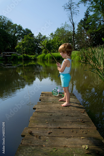 Little Boy Standing on Wooden Dock and Fishing on Lake