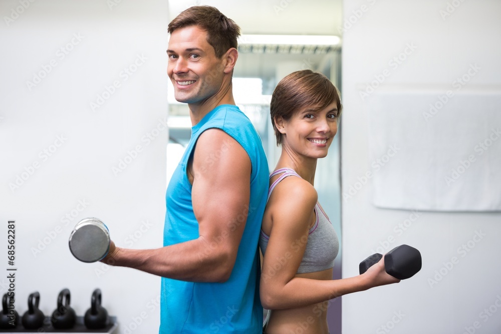 Obraz premium Fit couple lifting dumbbells together smiling at camera