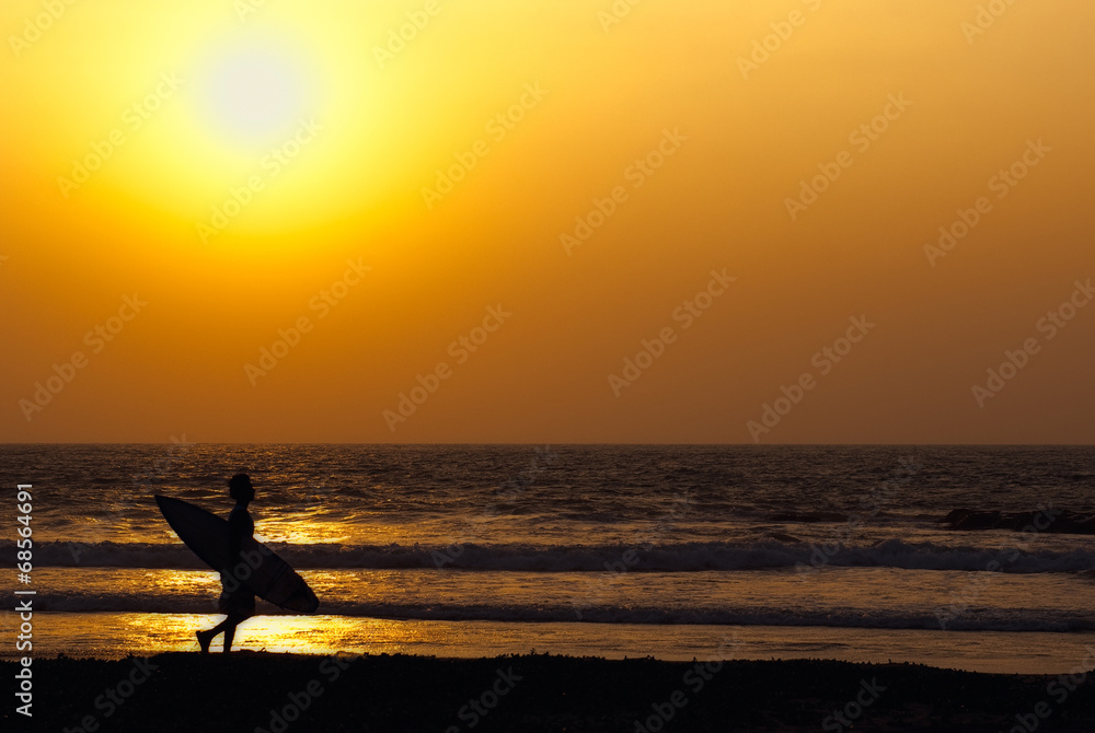 man walking along the coast with surfboard at the sunset