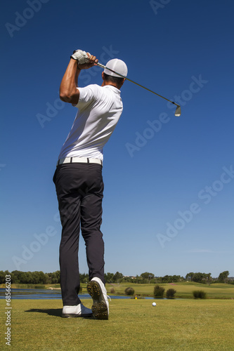 Golf player hitting a golf ball in a beautiful golf course.