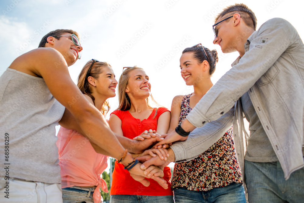 group of smiling friends with hands on top in city group of smiling friends with hands on top in city