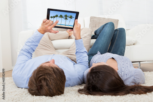 Couple Looking At Beach Photo On Digital Tablet
