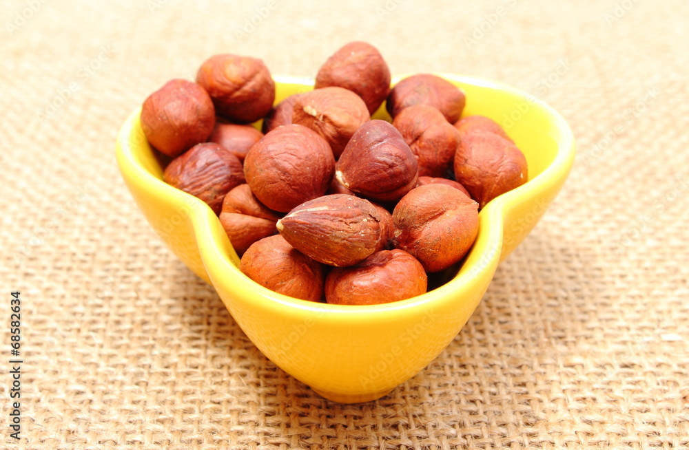 Fototapeta premium Heap of hazelnut in yellow cup on jute canvas