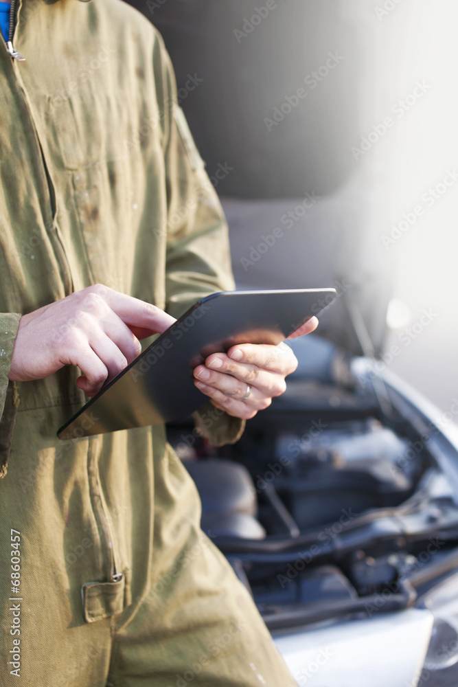 Mechanic using tablet computer wearing overalls under open hood