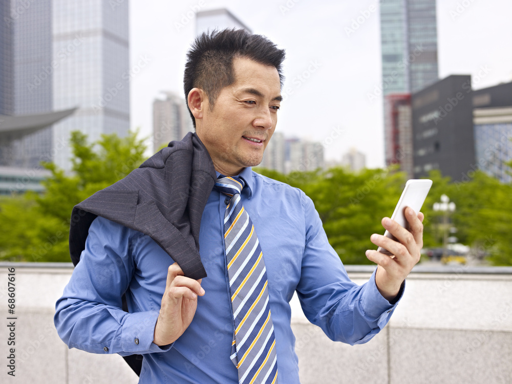 asian business executive looking at cellphone outdoors asian business executive looking at cellphone outdoors