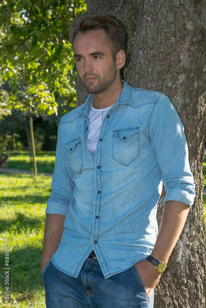 Young man standing at tree in park in summer Young man standing at tree in park in summer