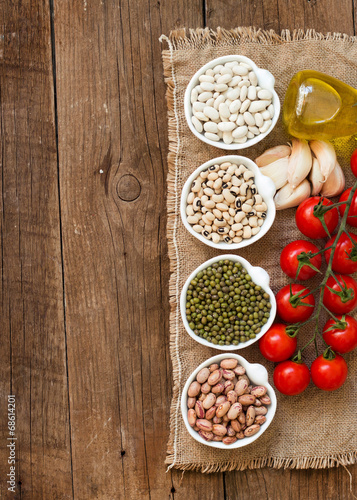 Legumes in bowls, tomatoes, garlic and olive oil on wooden table