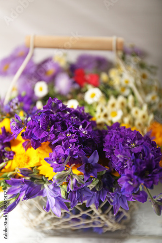 Beautiful wild flowers in basket on wooden background