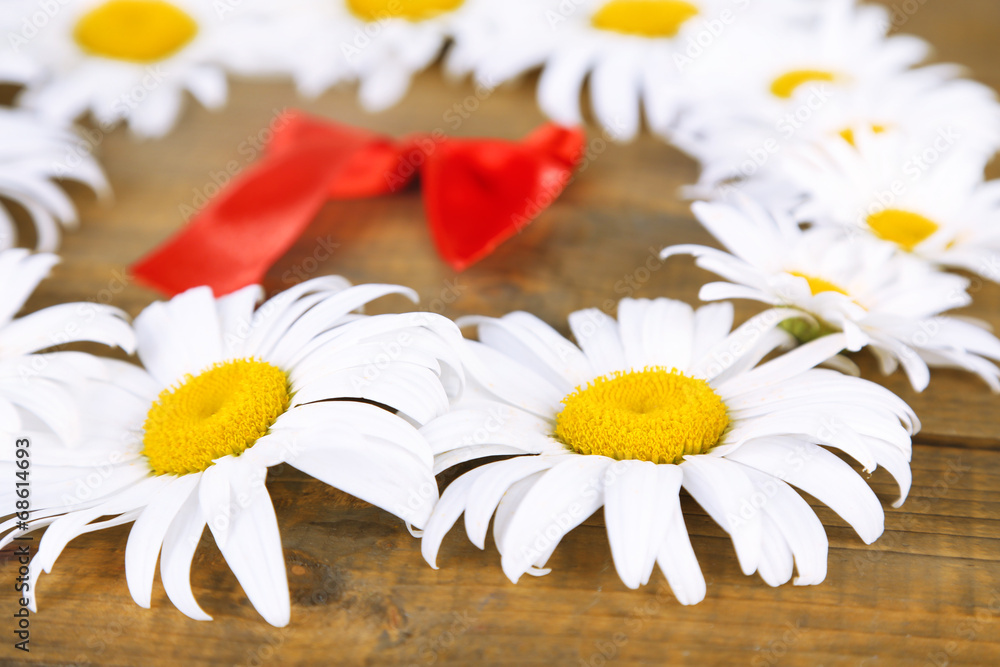 Obraz premium Chamomile wreath with red ribbon on brown wooden background