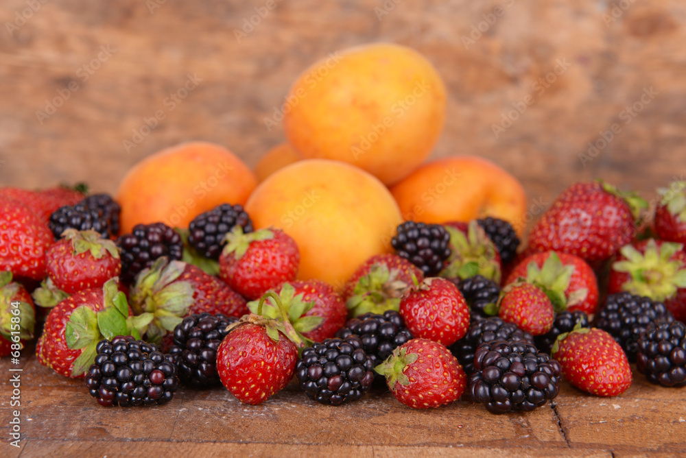 Ripe apricots and berries on wooden background