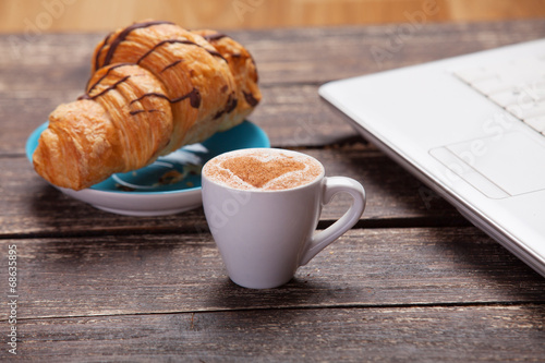 Fototapeta Naklejka Na Ścianę i Meble -  Croissant and cup of coffee with laptop on wooden table.