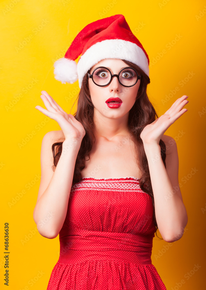 Beautiful brunette girl in christmas hat with glasses on yellow Beautiful brunette girl in christmas hat with glasses on yellow