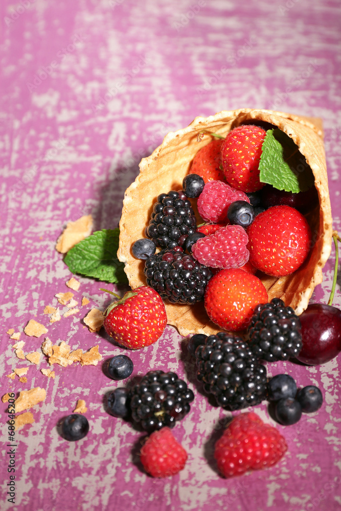 Different ripe berries in sugar cone, on purple background