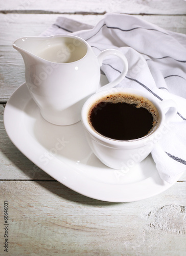 Cup of coffee, creamer on color wooden background