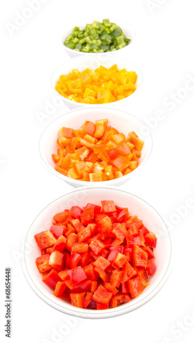 Colorful chopped capsicums in white bowls over white background