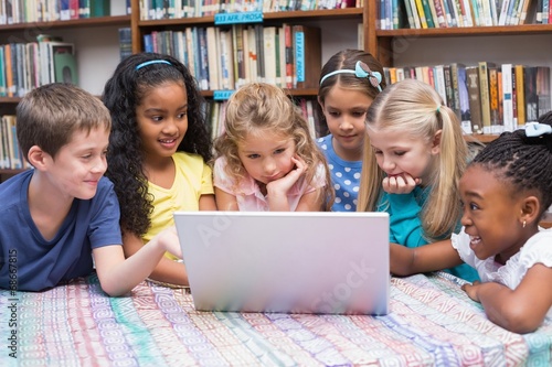 Cute pupils looking at laptop in library