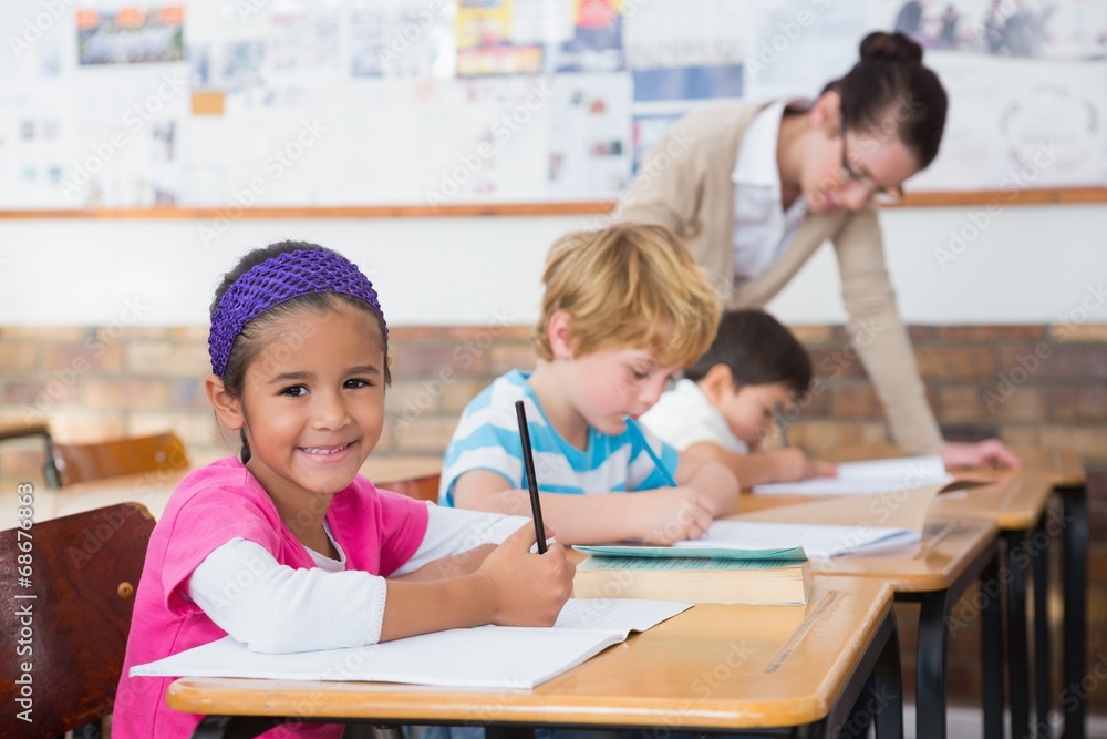 Cute pupils drawing at their desks one smiling at camera Cute pupils drawing at their desks one smiling at camera