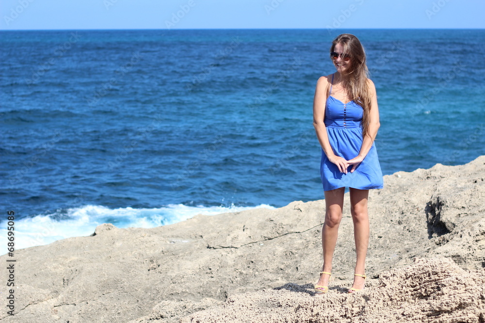Beautiful young woman with blue dress posing near the beach