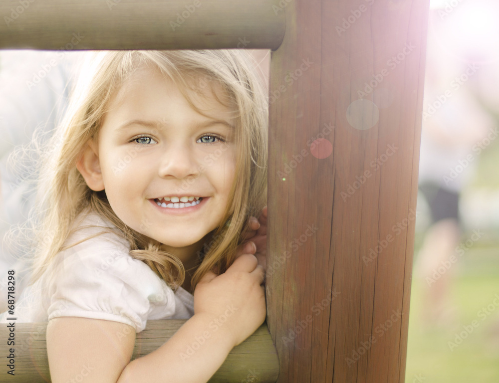 uśmiechnieta dziewczynka na tle drewnianego ogrodzenia - obrazy, fototapety, plakaty 