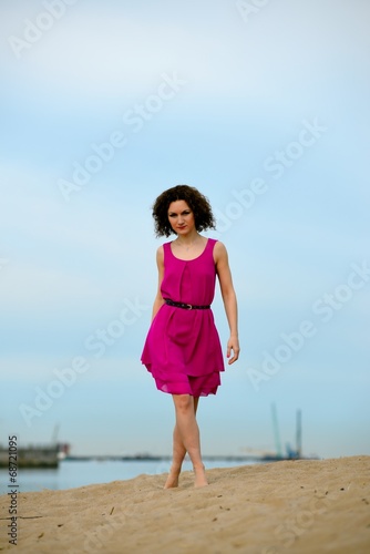 Young woman in a red dress and curly hair on the water coast