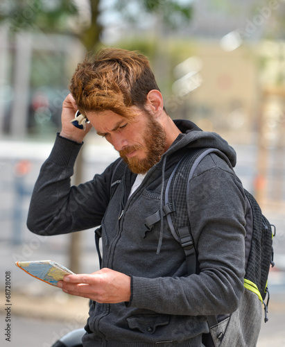 Lost bearded male tourist holding a map and gesturing with hands