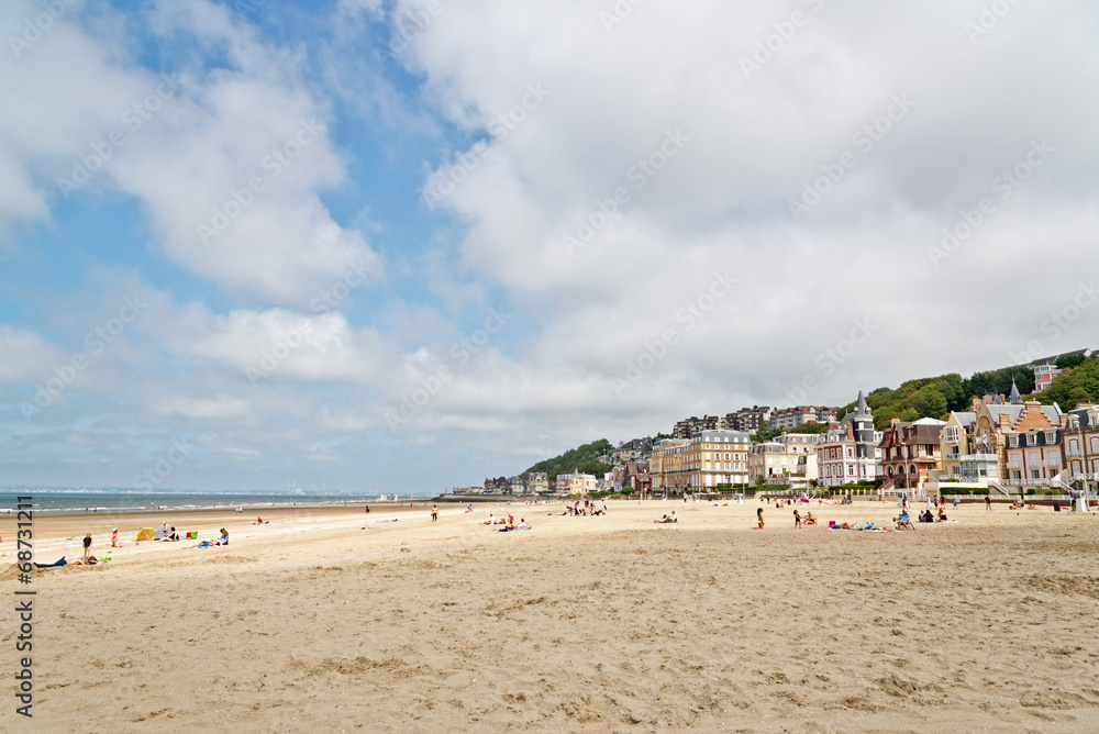 Beach with tourists and houses at Deauville with blue cloudy sky Beach with tourists and houses at Deauville with blue cloudy sky