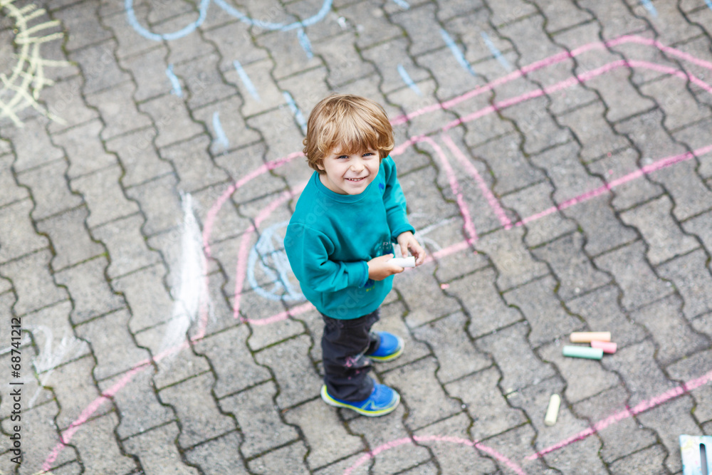 Little blond boy painting with colorful chalks outdoors