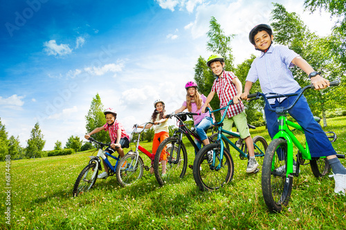 Row of children in colorful helmets holding bikes photo